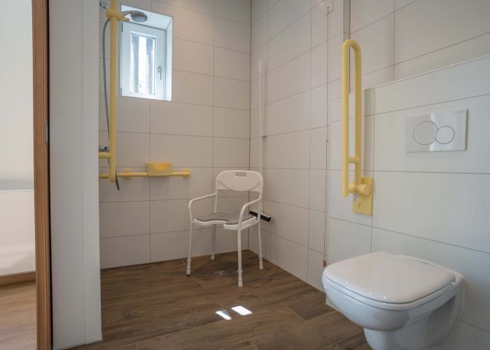 Modernes barrierefreies Badezimmer mit bodengleicher Dusche, Haltegriffen, Duschstuhl und WC.