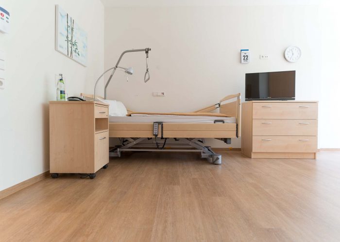 Helles Patientenzimmer der Winkelwaldklinik Nordrach mit Pflegebett, Nachttisch, Kommode und Fernseher.